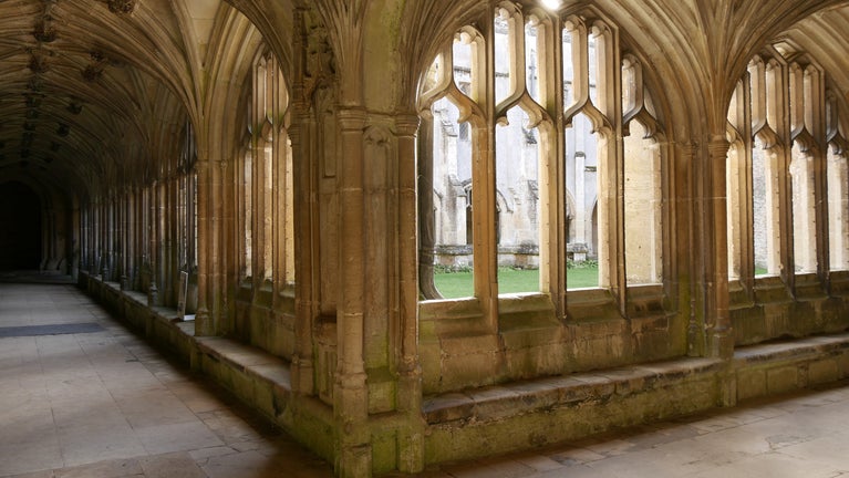 Looking down the Cloister walk at Lacock Abbey as light shines through the window, casting shadows on the floor.